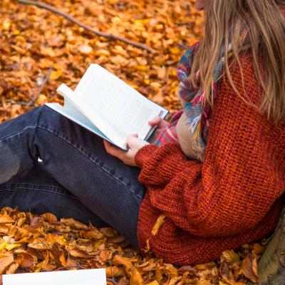 white teen reading outside in orange sweater surrounded by leaves