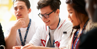 three teens gathered laughing mid-speech at a table wearing blue lanyards